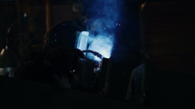 Koruyucu maskeli kaynakçı kaynak makinesiyle çalışıyor. Endüstriyel fabrikada metal kaynak yaparken kıvılcım ve duman üretiyor.
