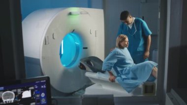 Yetişkin, beyaz bir kadının MRI kapsülüne uzanmış, elinde uzaktan kumandalı erkek radyoloji teknisyeninin görüntüleme prosedürünü açıklarken görüntüsü.