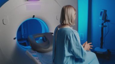 Hastanede tıbbi görüntüleme işleminden geçtikten sonra MRI teşhis odasında oturan, hastane önlüklü, sarışın, beyaz bir kadının orta boy fotoğrafı.