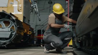 Siyahi kadın tamirci, endüstriyel fabrikada çalışırken sürekli iz bırakan makinenin tekerleğini tamir ediyor ve alnını siliyor.