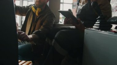 Kafkasyalı erkek tamirci, Afrikalı Amerikalı kadın meslektaşına, traktör kabininde oturup fabrikada çalışırken dijital tablet kullanmayı öğretiyor.