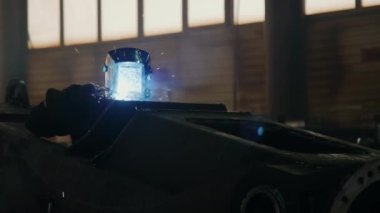 Fabrika işçisi koruyucu kalkanda alev ve kıvılcımlar üreterek metal parçaları kaynak yapıyor.