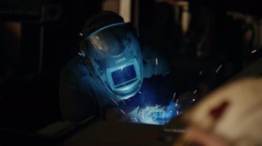 Metal işçisinin güvenlik maskeli görüntüsü demir kaynaklarını kaynak yaparken endüstriyel fabrikada kıvılcımlar üretiyor.
