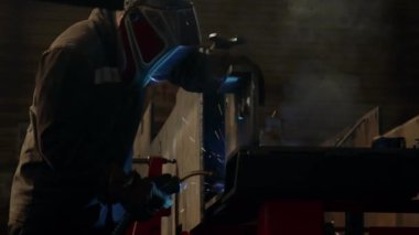 İş kıyafetleri ve koruyucu yüz kalkanı metallerinde çalışan erkek kaynakçı endüstriyel fabrikada kaynak makinesiyle çalışıyor.