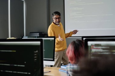 Modern bilgisayar bilimleri öğretmeni modern sınıfta öğrencilerin önünde duruyor ve ders veriyor.