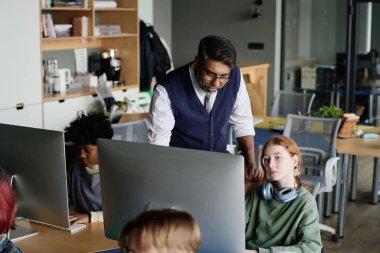 Bilgisayar bilimleri öğretmeninin genç öğrencilere kodlama konusunda yardım ettiği yüksek açılı bir çekim.