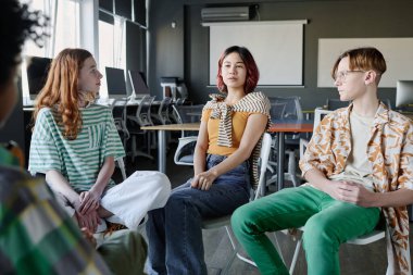 Asyalı genç kız okulda grup terapisi sırasında sorunlarını anlatırken sandalyede oturuyor.