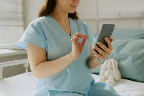 stock image Pregnant woman sitting on hospital bed and smiling while she checking her phone