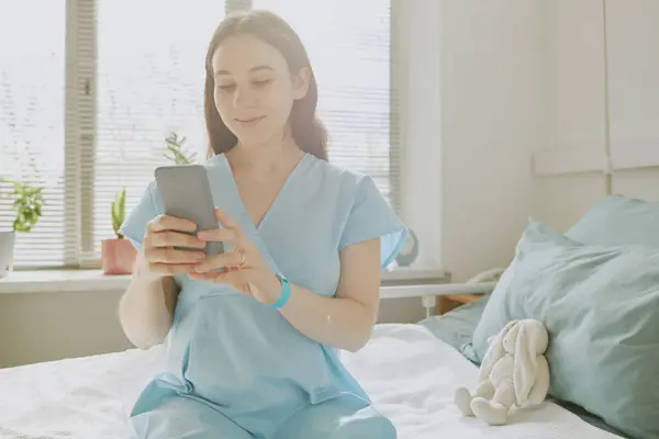 stock image Young pregnant woman chatting via phone while staying at maternity hospital