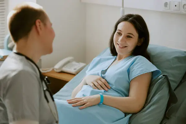 stock image Pregnant woman lying on hospital bed and looking at nurse with wide smile