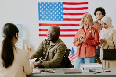 Tekerlekli sandalyedeki neşeli Afrikalı Amerikalı adam seçim günü oy pusulasında oy kağıdı alıyor, boşluğu kopyalıyor.