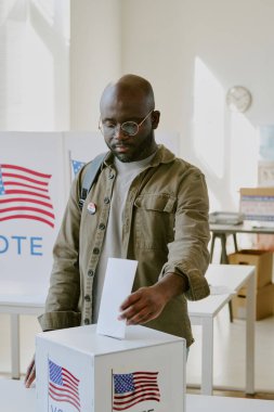 Genç Afro-Amerikan erkek vatandaşının seçim günü oy sandığına oy kağıdı koyduğu dikey kare.