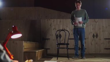 Sahnede yürüyen, kadın yönetmenle konuşan ve tiyatro seçmelerinde rol alan genç bir aktörün omuzlarının üzerinden.