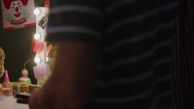 Orta yaşlı beyaz erkek sirk sanatçısı soyunma odasına giriyor ve boya kullanarak palyaço makyajı yapmaya hazırlanıyor.