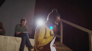 Sahnede tiyatro grubuyla prova yaparken gülümseyen ve duygusal konuşmalar yapan genç siyahi aktris.