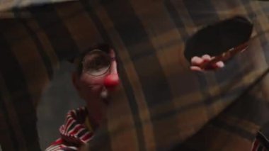 Siyah bereli, yuvarlak gözlüklü, sirkte gösteri yapan, yüzünü buruşturan ve kamerada delikler açan beyaz erkek palyaço portresi.