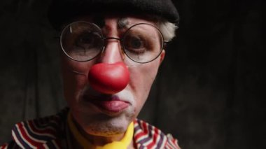 Sirkte palyaço kıyafeti ve kırmızı burunlu, suratını ekşiten ve kameraya aptal suratlar yapan olgun, beyaz bir adamın yakın plan portresi.