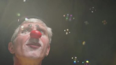 Sirk gösterisi sırasında palyaço rolü yapan, sabun köpüklerini yakalayıp patlatmaya çalışan odaklanmış orta yaşlı beyaz adamın yakın çekimi.