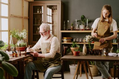 Kadın parfümcü papatya buketi keserken son sınıf erkek parfümcü masada oturuyor ve not alıyor.