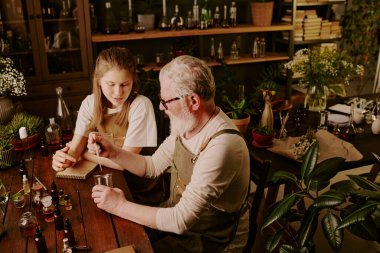 Olgun bir parfümcü, genç bayan stajyerine parfüm üretme sürecini gösterirken aromasına ekstra gerekli yağı ekler.