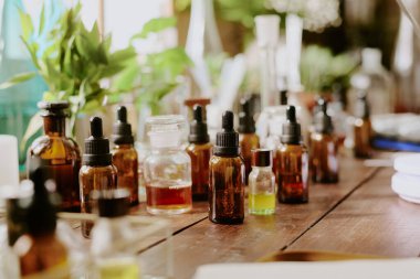 Orta boy cam şişeler aromatik sıvı ve şeffaf şişeler ile karamel ve altın rengi esans antik ahşap masa üzerinde, yeşil ev bitkileri arka planda