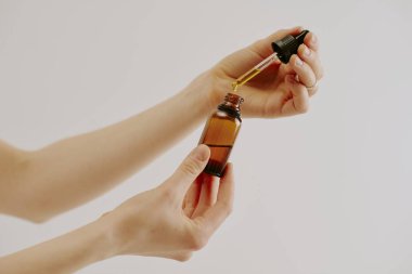 Kahverengi cam şişe ve organik altın esansla dolu cam pipet tutan kadın elleri.