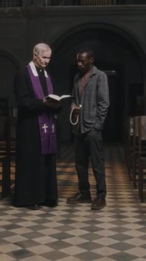 Kafkas rahiplerinin Afrika kökenli Amerikalı erkek cemaate İncil verip onunla kilisede konuştuklarının dikey görüntüsü.