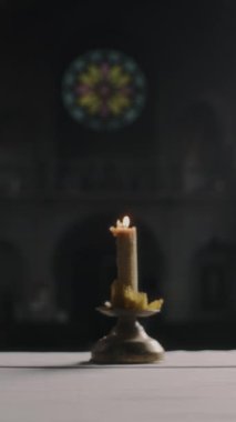 Koyu gotik bir katedralde, pirinç tutacağında yanan mumun dikey yakın çekimi.