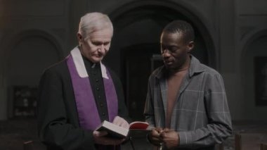 Geleneksel cüppeli Kafkas rahibi İncil veriyor ve kiliseyi ziyaret eden siyahi cemaatle konuşuyor.