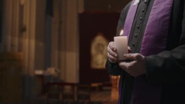 Siyah cüppeli ve mor atkılı rahibin kilisede mum ışığı tuttuğu orta bölüm çekimini kapat.