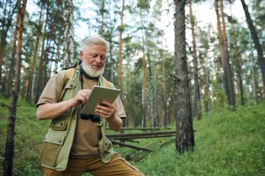 Açık havada çalışırken dijital tablet kullanan, yüzleri sakallı, modern Kafkasyalı ormancı.