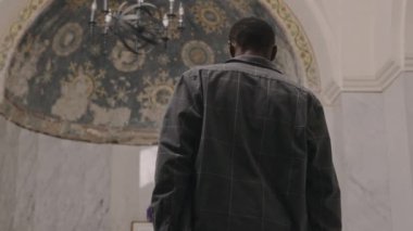 Kilisede mermer duvarlar ve boyanmış tavanla yürüyen, mihraba yaslanan ve dua eden Afrikalı Amerikalı cemaatin arka görüntüsü.
