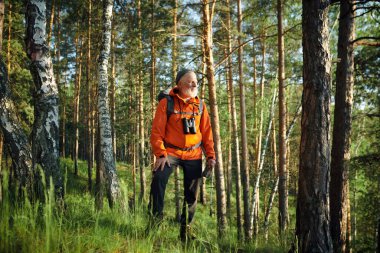 Turuncu ceketli, kendinden emin beyaz erkek turistin dağ ormanlarında elinde kağıt haritayla durduğu geniş bir kare.