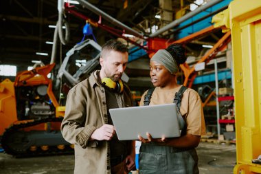 Çift ırklı erkek ve kadın fabrika işçilerinin laptop ekranına bakıp yeni makine tasarımını tartışırken orta boy görüntüsü.