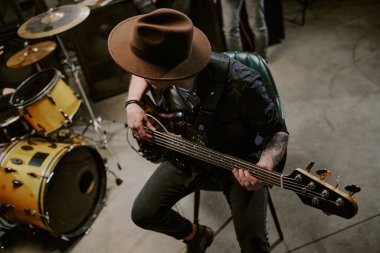 Yüksek açılı, şapkalı, sandalyede oturan, bas gitar çalan, uzayı kopyalayan tanınmamış bir adamın görüntüsü.