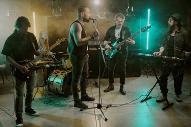 Gece kulübünde modern X jenerasyonu erkek ve kadın rock müzisyenlerinin sahnede şarkı söylemesinin uzak bir çekimi.