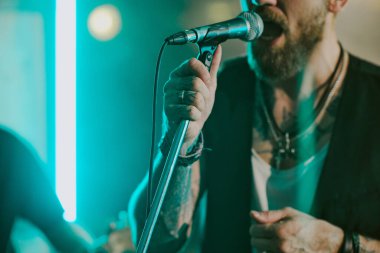 Mikrofon taşıyan sakallı adamın sahnede rock şarkıları söyleyip, uzayı kopyaladığı orta boy yakın plan.