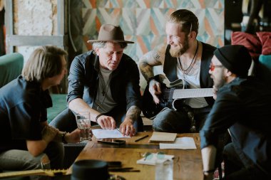 Group of gen X rock musicians sitting at vintage coffee table in their studio in abandoned building writing new song clipart