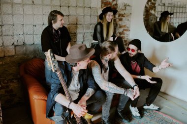 Group of male and female rock musicians sitting on leather couch having conversation during photoshoot for new album clipart