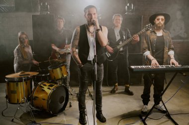 Modern rock grubunun mikrofon ve müzik enstrümanlarıyla kameraya poz vermeye hazır uzak çekimi.