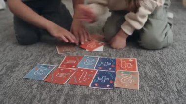 Beyaz tenli genç kız ve oğlanın çocuk odasında halı döşemesinde oturup sayısal kart oynadığı ve görevi tamamladıktan sonra birbirlerine beşlik çaktıkları yakın çekim.