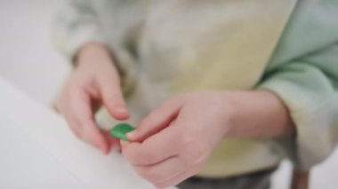 Küçük yeşil bir parça plastik tutarak, yoğurarak, düzleştirerek ve sanat dersinde heykel yapmaya hazır hale getirerek tanınamaz hale gelmiş genç çocukların elleri.