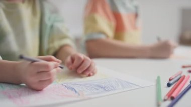 İki beyaz anaokulu öğrencisinin resim dersinde mum boya kalemleri ve renkli kalemler kullanarak anaokulundaki masalarında sessizce oturması.