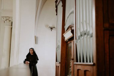 Katolik katedralindeki boru orgu yakınında duran düşünceli Kafkas rahibesi, boşluğu kopyala