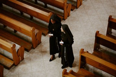 Etnik açıdan farklı iki genç ve olgun Katolik rahibenin saf bir şekilde yürüyüp sohbet etmesinin yüksek açılı görüntüsü.