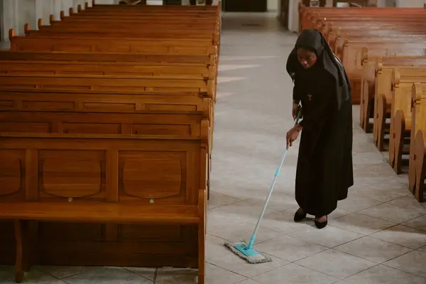 stock image High angle view long shot of young African American Catholic nun wiping floor at nave in cathedral, copy space