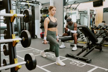 Çaylak halter sallarken Afrika kökenli Amerikalı erkek koçu bankta oturup telefonda antrenman rutinini yazıyor.