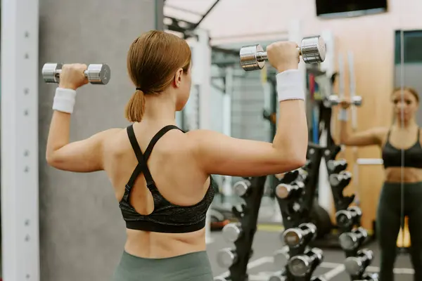 stock image Woman looking in mirror and watching her exercise technique while she doing dumbbell shoulder press