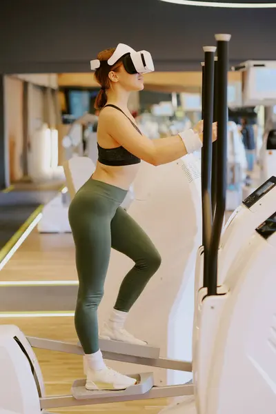 stock image Woman warming up on elliptical machine before workout, she playing VR online game