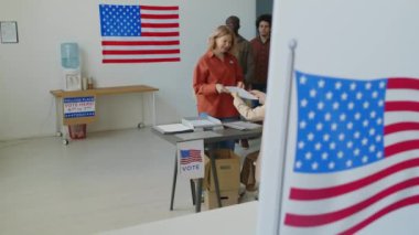Çeşitli Amerikan vatandaşları kadın seçim müfettişlerinden oy pusulaları alıyor ve oy kullanma yerlerine gidiyorlar.